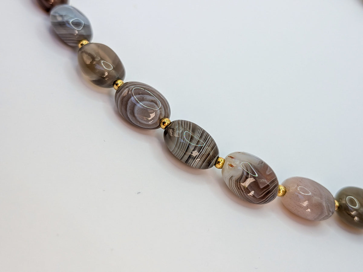 Gros plan sur les rubans naturels gris, bruns et blancs des perles ovales du collier en agate du Botswana.