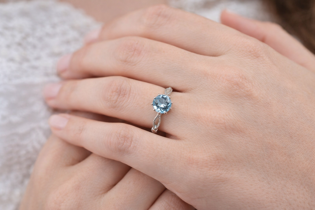 Bague Célestine Ecrelya Prestige portée à la main, topaze bleue naturelle ronde, argent 925 finition or blanc PVD.