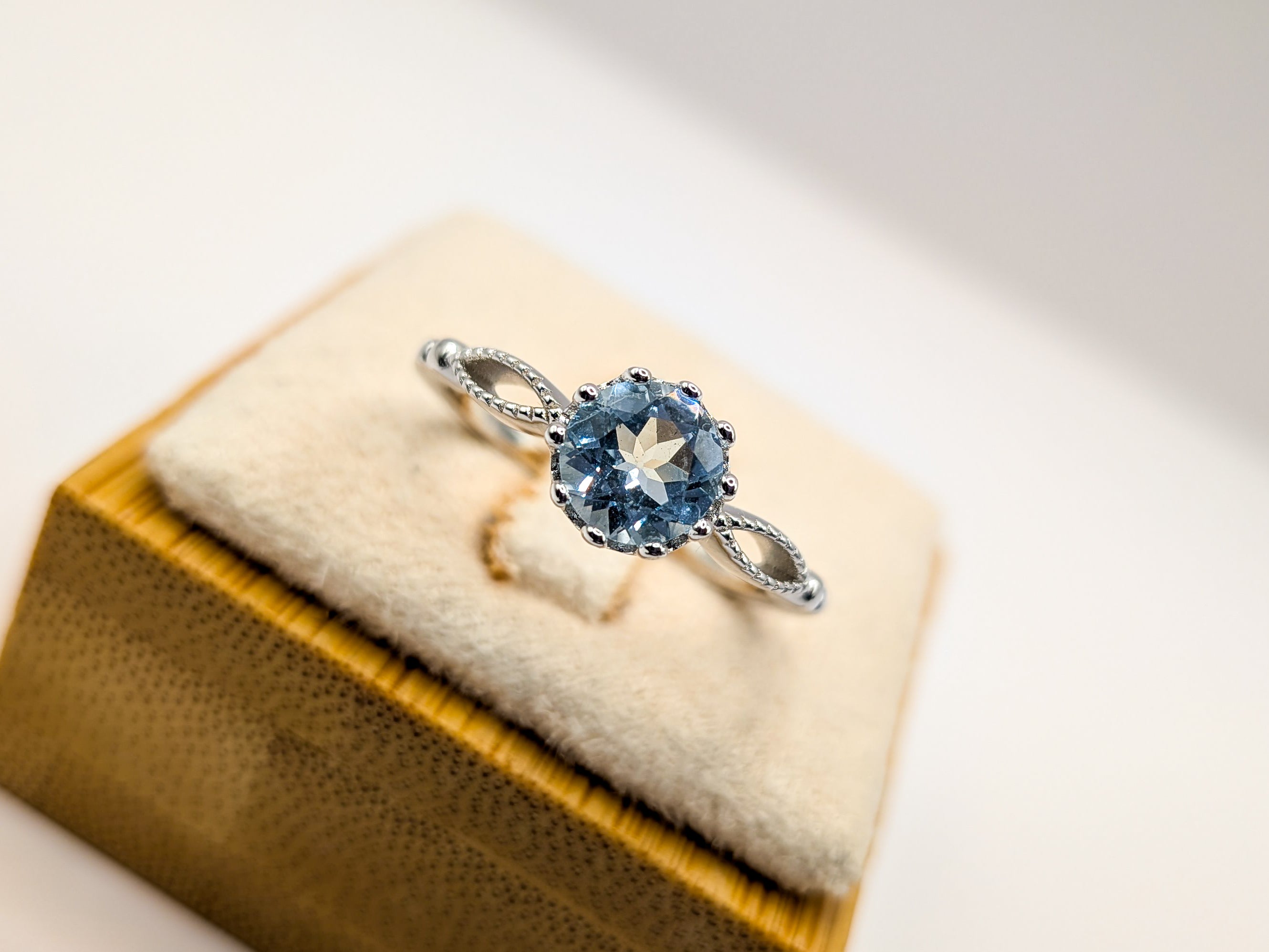 Gros plan sur topaze bleue naturelle facettée, sertie griffes sur bague en argent 925 finition or blanc PVD.