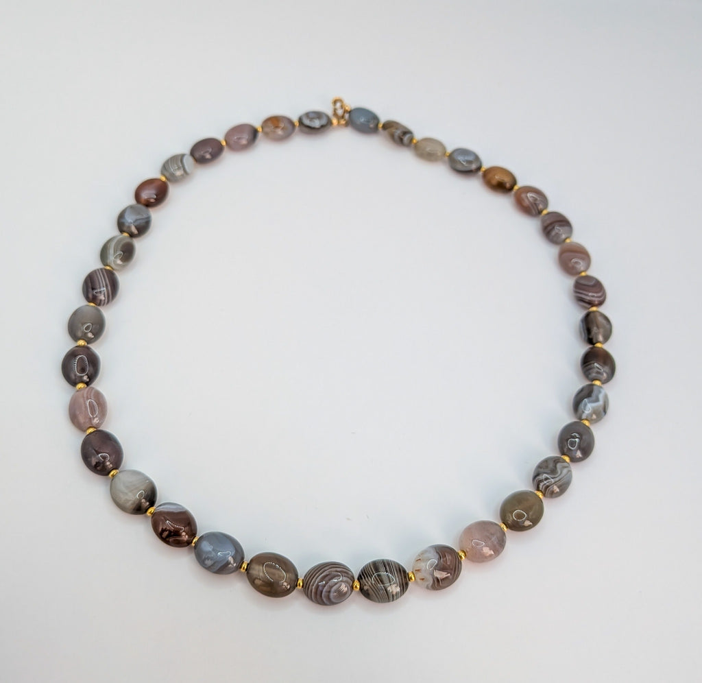 Collier Ecrelya en agate du Botswana, perles ovales grises et brunes séparées par de petites perles dorées.