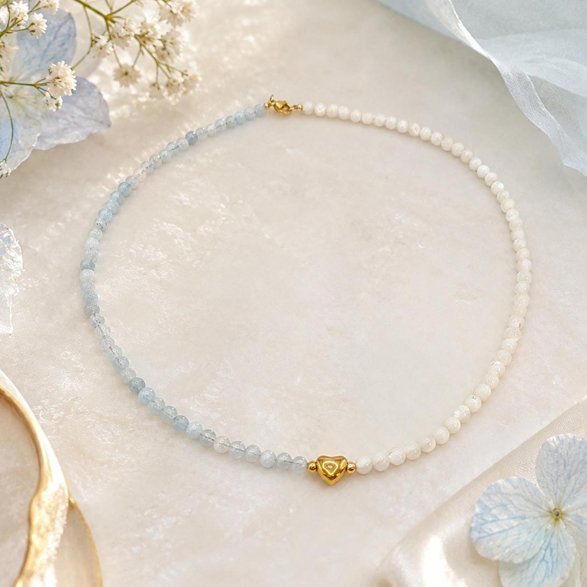 Vue complète du collier asymétrique aigue-marine et nacre sur une pierre claire