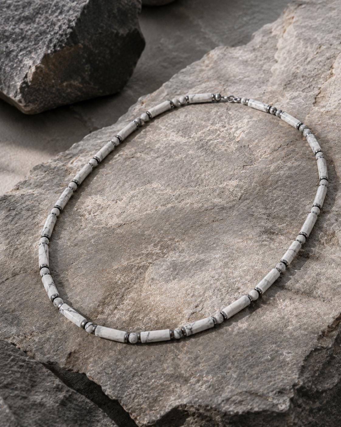 Collier howlite blanche et hématite argentée posé sur une roche grise