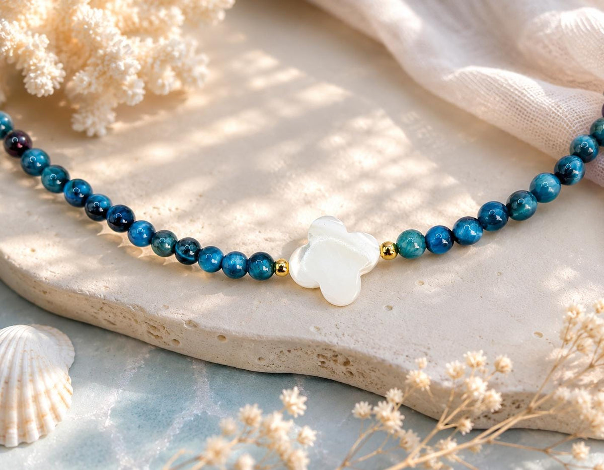 Collier œil de tigre bleu posé sur une pierre claire avec son trèfle nacré